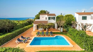 Una casa de dos pisos con piscina, zona de estar exterior y vista al mar.