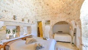 A stone-walled bedroom with a bed, a small table, and a mirror.