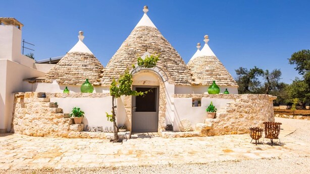A traditional stone house with three conical roofs, a central door, and potted plants.