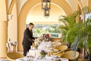 A well-set dining area with tables, wicker chairs, and a waiter serving.
