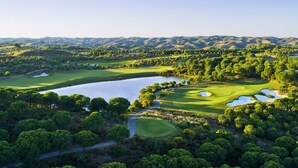 Ein Golfplatz mit einem See, umgeben von dichten Bäumen und sanften Hügeln.