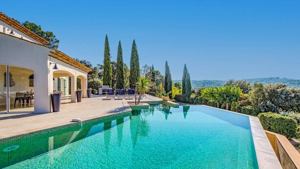 A swimming pool with a clear blue water, surrounded by a patio area with chairs and a table, and tall cypress trees in the background. - Villa Les Etoiles by Villa Plus (Lorgues)