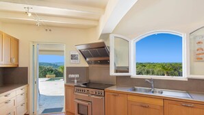 A modern kitchen with a built-in oven, stovetop, and a large window offering a view of the outdoors. - Villa Les Etoiles by Villa Plus (Lorgues)
