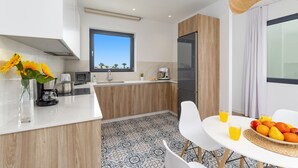 Een moderne keuken met een groot raam, een eethoek met een tafel en stoelen, en een fruitschaal met sinaasappels en citroenen.