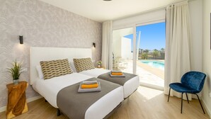 Een moderne slaapkamer met een groot bed, een klein tafeltje, een stoel en uitzicht op een zwembad.