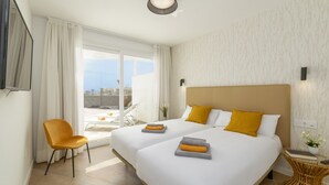 Een hotelkamer met twee bedden, een stoel, een tafeltje en uitzicht op buiten.