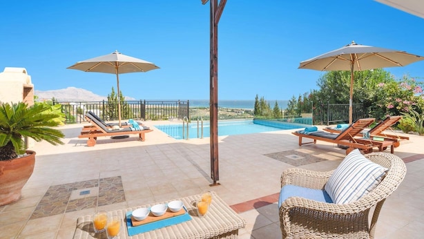 Ein Poolbereich mit Liegestühlen, Sonnenschirmen und Blick auf das Meer.