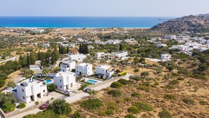 Eine Vogelperspektive auf die Villa Petalouda, mit modernen weißen Gebäuden, einem Swimmingpool und einer Küstenlandschaft im Hintergrund.
