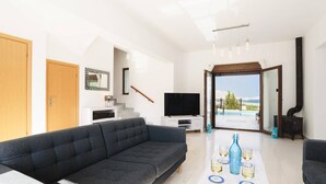 Ein modernes Wohnzimmer mit grauem Sofa, einem Flachbildfernseher und einem Esstisch mit Obst und Gläsern.