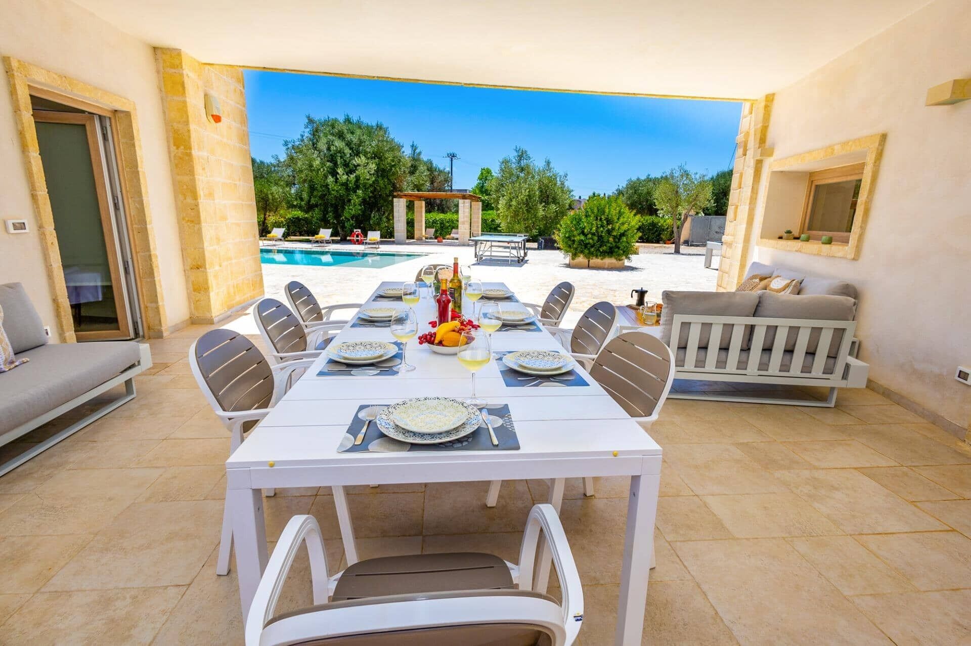 Un espace repas avec vue sur la piscine, des sièges d’extérieur et un mur en pierre.