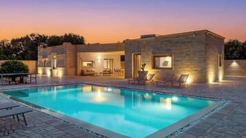 Eine moderne Villa mit Swimmingpool, Sitzgelegenheiten im Freien und Steinarchitektur.