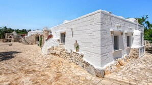 A white stone building with a stone-paved courtyard, featuring arched doorways and windows.