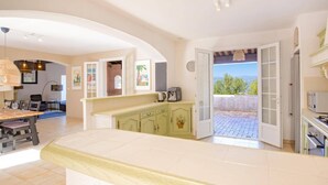 Una cocina amplia con una isla grande, un comedor con mesa y sillas, y vista al exterior a través de una puerta abierta.