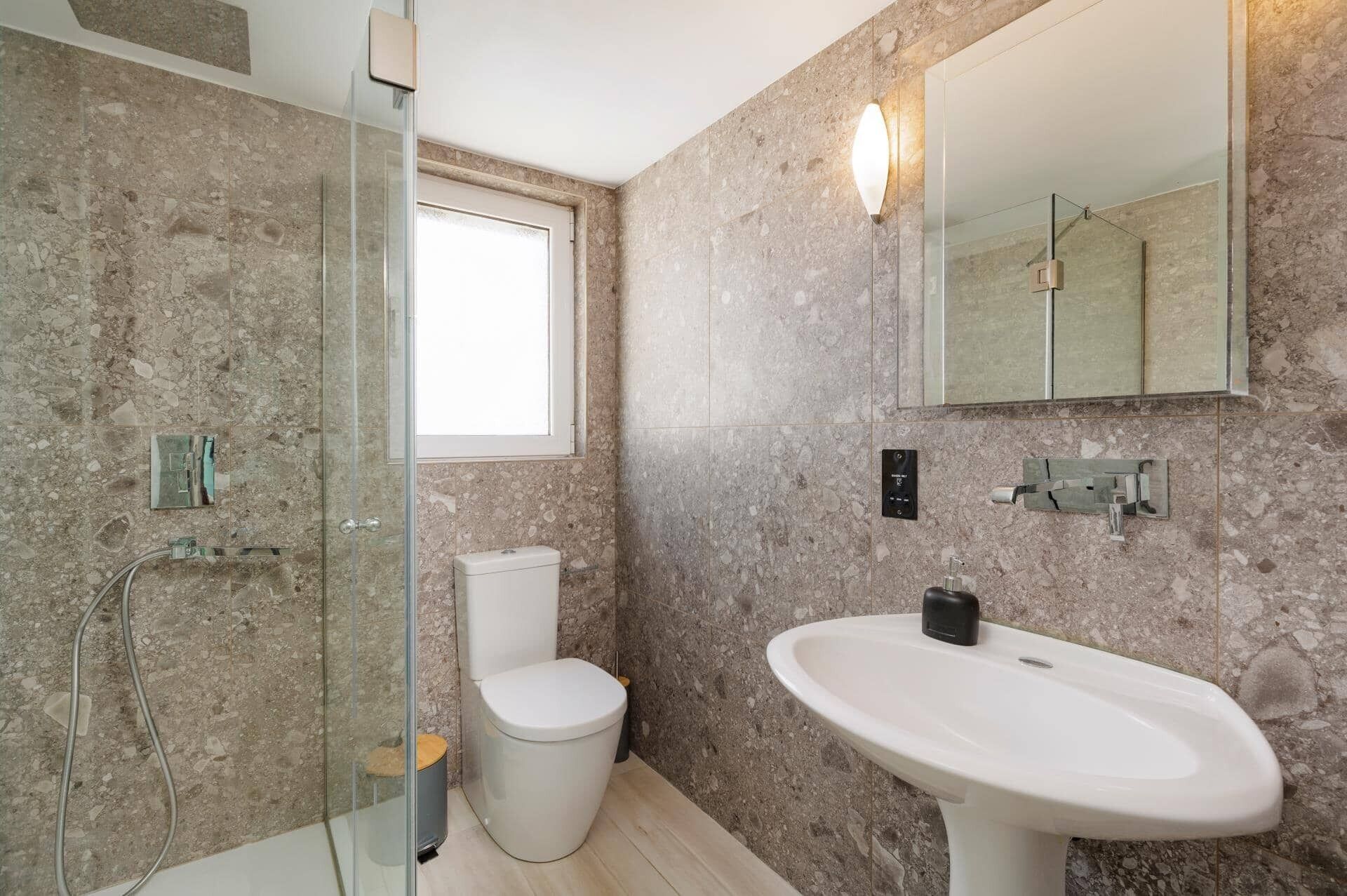Une salle de bain avec une douche à parois de verre, des toilettes, un lavabo et un miroir.