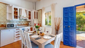 Une cuisine avec des meubles blancs, un four à micro-ondes et une table à manger dressée pour deux personnes, avec des assiettes, des verres et un vase de fleurs.