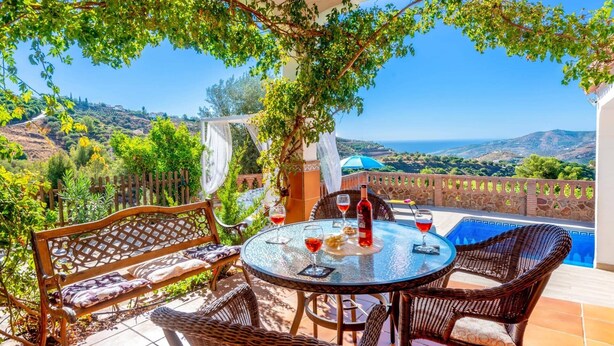 Une terrasse dotée de meubles en osier, d’une table en verre et offrant une vue sur la mer.