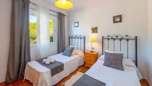 Une chambre avec deux lits simples, une table de chevet avec une lampe et une fenêtre avec des rideaux.