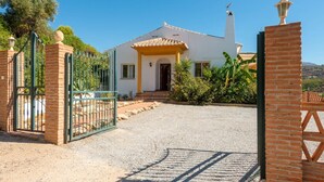 Une maison avec une allée en gravier, une entrée fermée par un portail et un ciel d’un bleu éclatant.