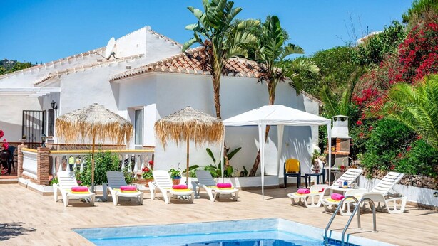 Un espace piscine avec des chaises longues, une tente blanche et un bâtiment doté d’un toit en tuiles.