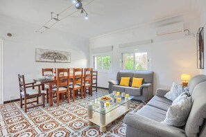 Una sala de estar con comedor, un sofá gris con cojines amarillos, una mesa de centro de vidrio y baldosas de suelo estampadas.