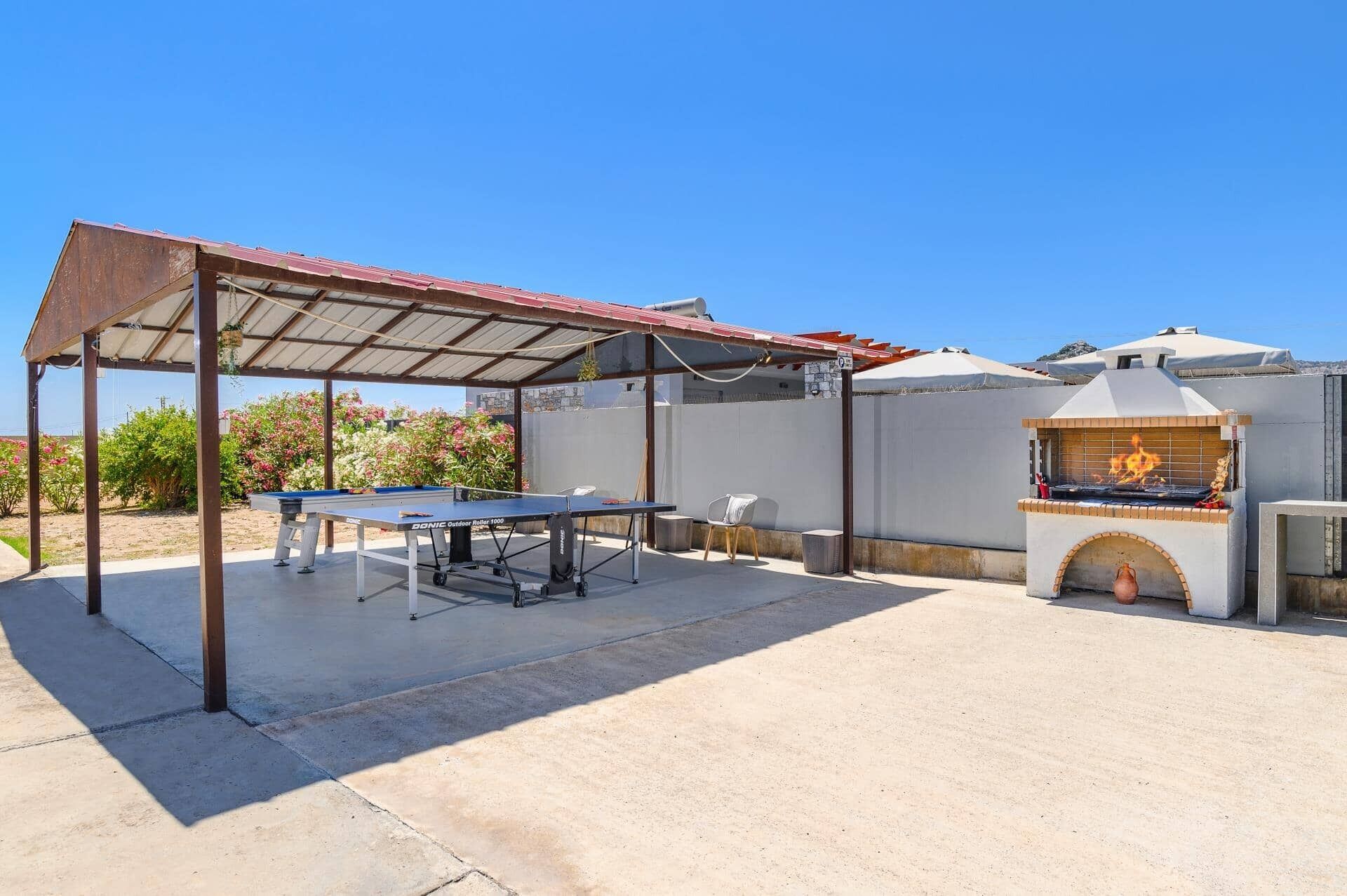 An outdoor patio with a ping pong table, a barbecue grill, and a covered seating area.