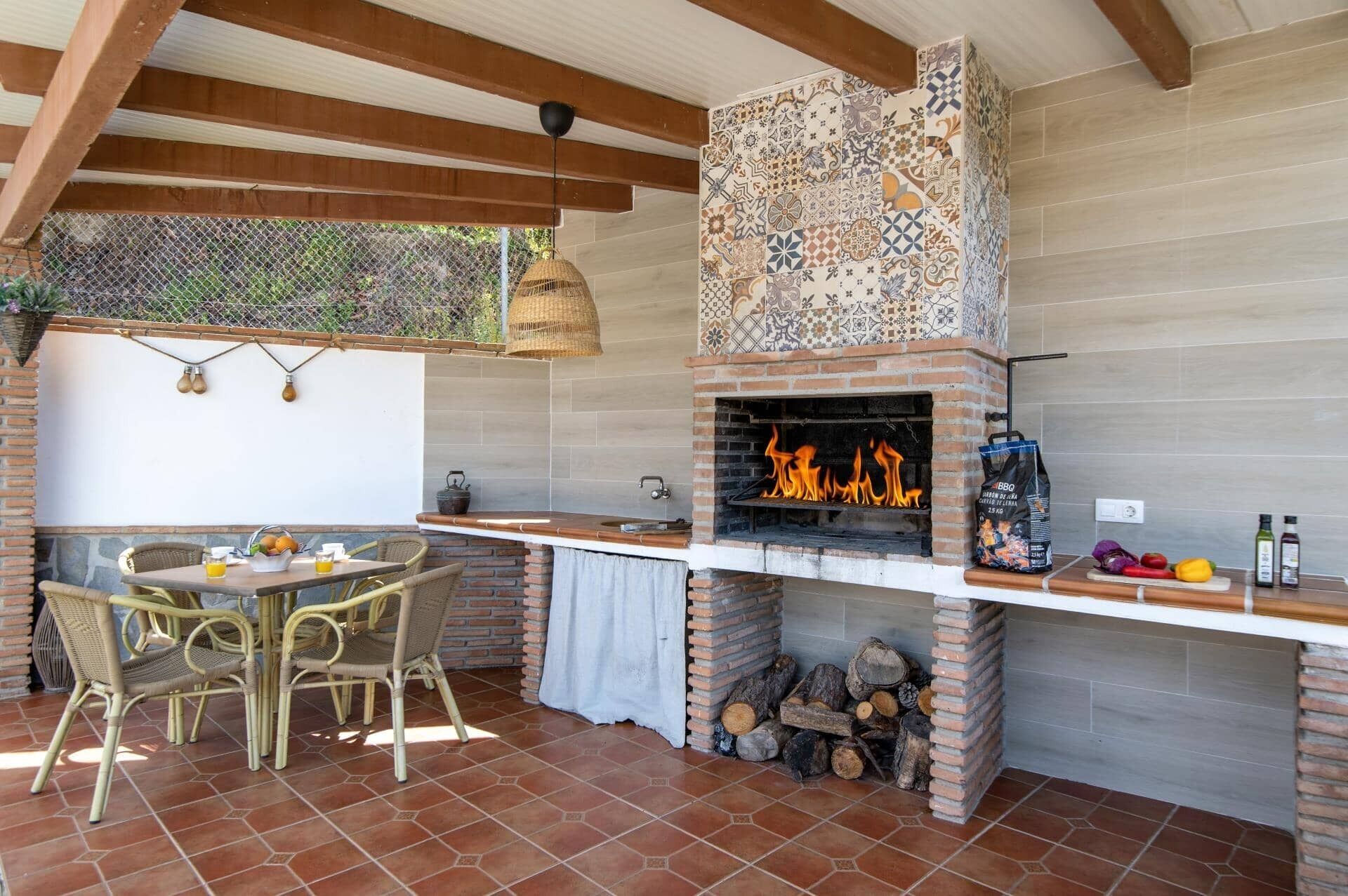 Una cucina esterna con forno in mattoni, sedie in vimini e pavimento piastrellato.