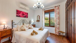 A bedroom with a bed, bedside tables, a chandelier, a window with curtains, and a wardrobe. - Villa Maravillas by Villa Plus (Frigiliana)