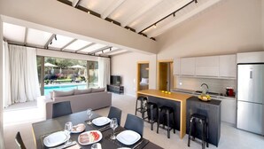 A modern kitchen with a dining area, a pool view, and a living area with a sofa. - Villa Masticha Sweet by Villa Plus (Kariotes)