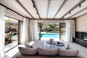 Een moderne woonkamer met een groot raam, een zwembad en tuinmeubilair.