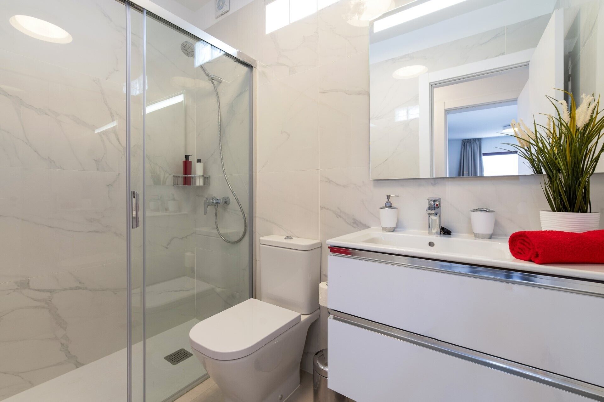 A modern bathroom with a glass-enclosed shower, a white toilet, and a vanity with a mirror.