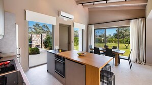 A modern kitchen with an island, a dining area with a table and chairs, and a view of a garden. - Villa Pasteli Sweet by Villa Plus (Kariotes)