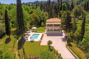 Una casa de dos pisos con piscina, rodeada de follaje y árboles.