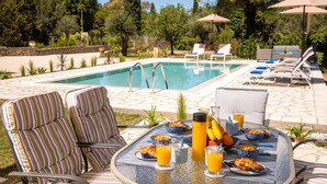 Desayuno junto a la piscina con sillones de descanso, una mesa con alimentos para el desayuno y una piscina.