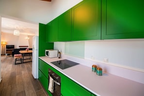 Een moderne keuken met groene kasten, een wit aanrechtblad en een ingebouwde oven. Op de achtergrond is een eethoek met een tafel en stoelen zichtbaar.