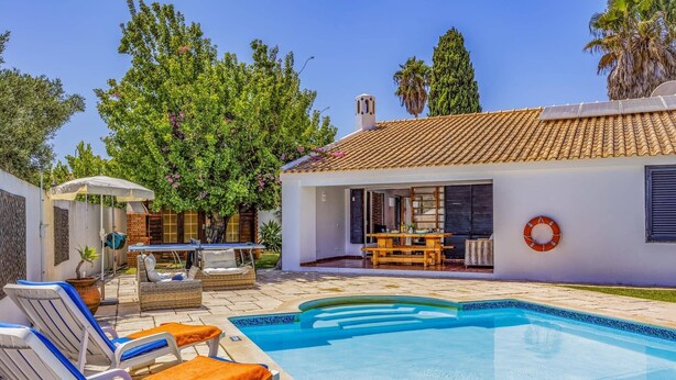 A swimming pool with lounge chairs, a dining area, and a covered patio. - Villa Damasco by Villa Plus (Albufeira)