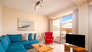 Una sala de estar moderna con un sofá azul, un sillón rojo, una mesa de centro de madera y un televisor sobre un mueble de madera.