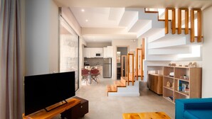 Una sala de estar moderna con un televisor de pantalla plana, muebles de madera, una escalera y una cocina al fondo.