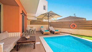 Un área de piscina moderna al aire libre con una mesa de madera, dos sillones de descanso y una sombrilla.