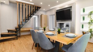 Un espace repas moderne avec une table en bois, des chaises grises et un escalier doté de rampes en bois et en noir.