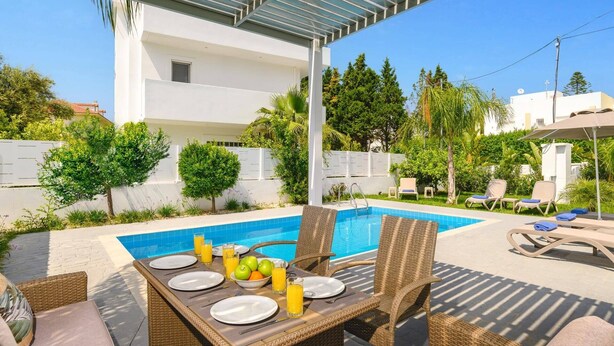 Un espace repas aménagé au bord de la piscine, avec des meubles en osier, une table dressée pour deux personnes et une piscine en arrière-plan.