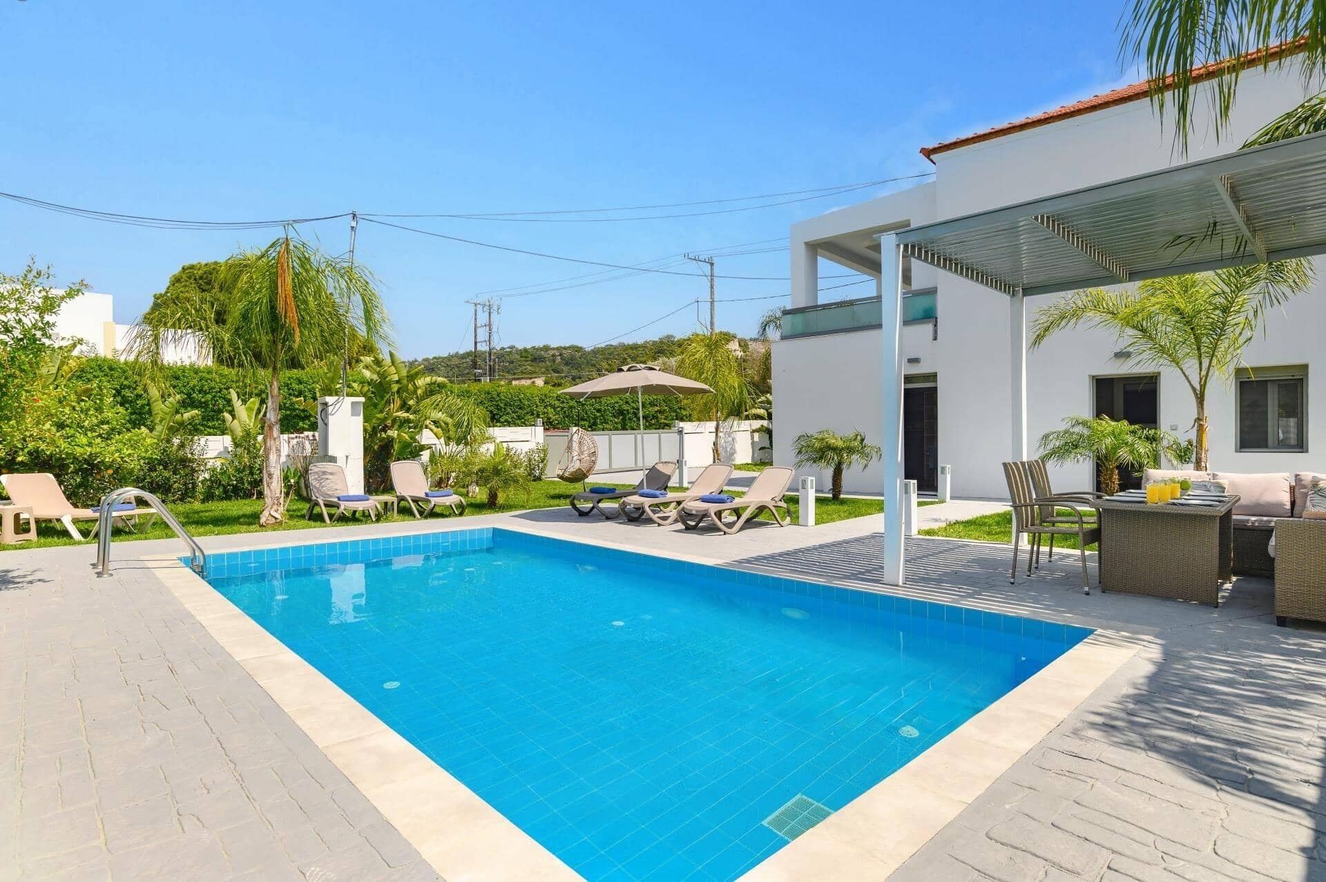 Une piscine avec des chaises longues, un espace de détente couvert et un bâtiment moderne en arrière-plan.