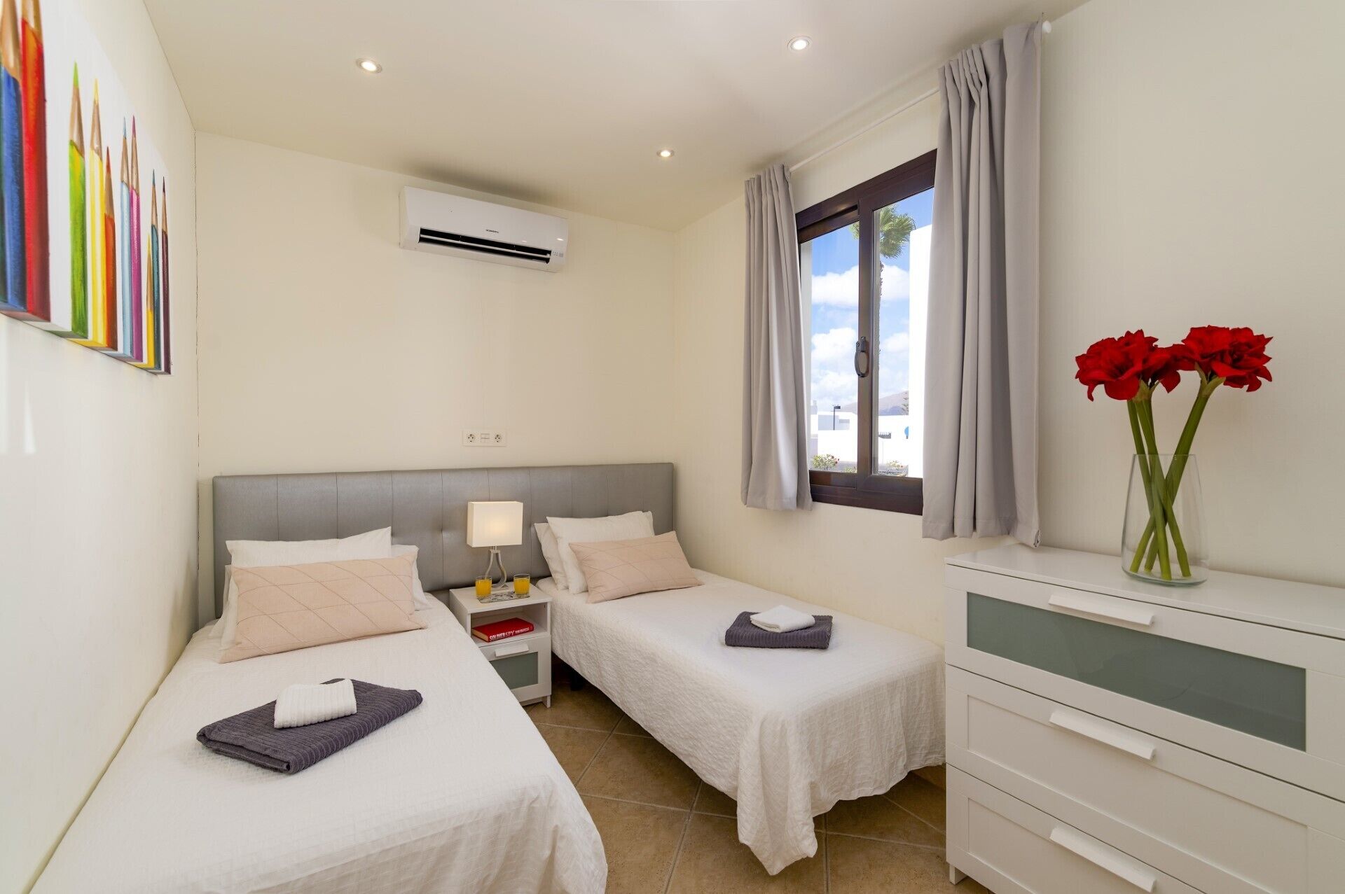 A hotel room with two beds, a bedside table with a lamp, a dresser, and a window with curtains.