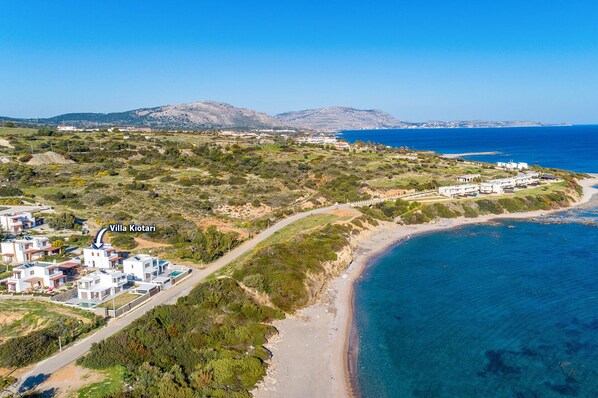 An aerial view of Villa Kiotari, featuring a coastal road, a beach, and surrounding greenery.