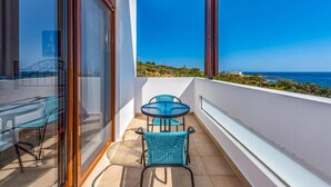 A balcony with a table and chairs, a view of the sea, and a building in the background. - Villa Kiotari by Villa Plus (Kiotari)