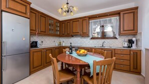 A kitchen with wooden cabinets, a stainless steel refrigerator, a dining table with chairs, and a fruit bowl. - Villa Kiotari by Villa Plus (Kiotari)