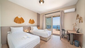 Een hotelkamer met twee bedden, een bureau en een balkon met uitzicht op zee.