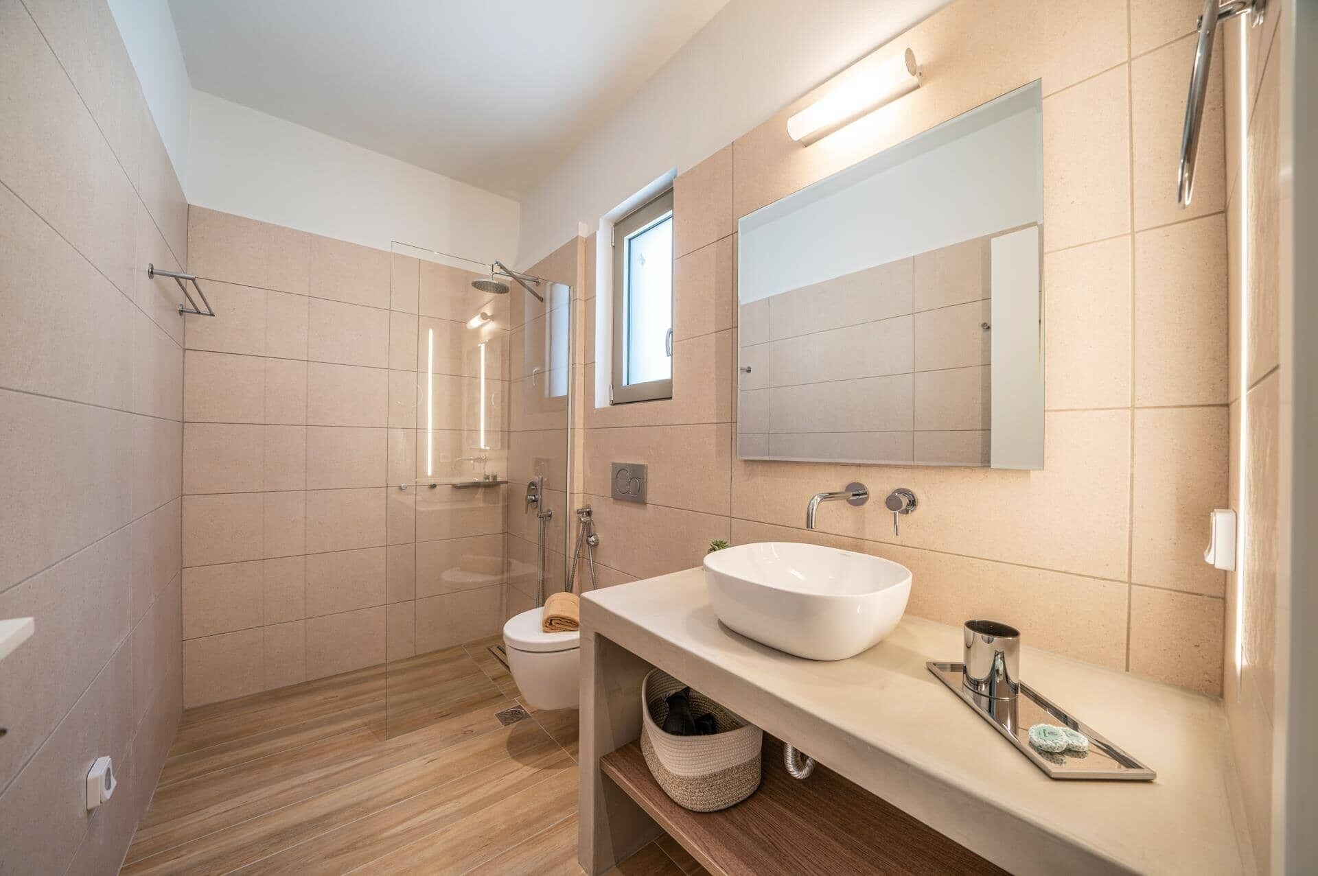 Un baño moderno con un espejo grande, un lavamanos blanco y una ducha con mampara de vidrio.