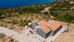 En modern villa med en swimmingpool, omgiven av ett kuperat landskap och med utsikt över havet.