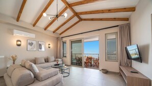 Een ruime woonkamer met een bank, een bijzettafeltje en een televisie op een houten dressoir. Er is een balkon met een tafel en stoelen, en een schuifdeur naar een terras.