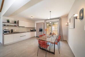 Une cuisine moderne avec un coin repas, comprenant une grande table, des chaises rouges et une vue sur l’extérieur grâce à une porte vitrée.
